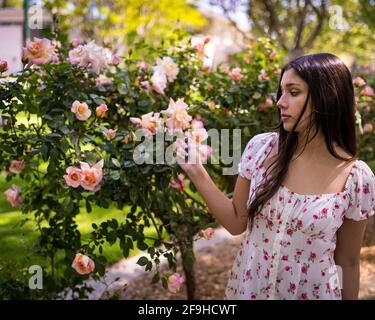 Schöne Latina Teen bewundern Rosen in einem Garten in lite Kleid für den Frühling Stockfoto