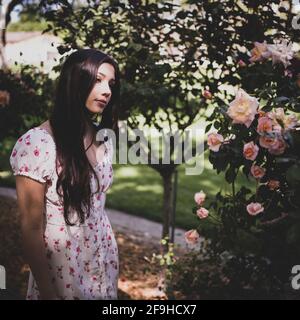 Schöne Latina Teen bewundern Rosen in einem Garten in lite Kleid für den Frühling Stockfoto