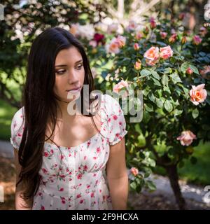 Schöne Latina Teen bewundern Rosen in einem Garten in lite Kleid für den Frühling Stockfoto