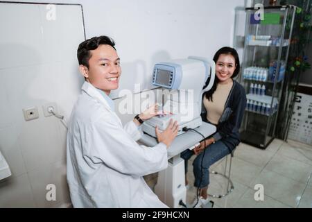 Ein männlicher Arzt hat die Untersuchung der Augen eines weiblichen Patienten beendet Mit einem Augencomputer Stockfoto