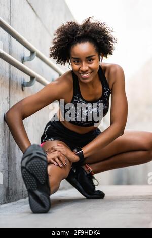 Afro-Athletin, die vor dem Training die Beine streckt. Stockfoto