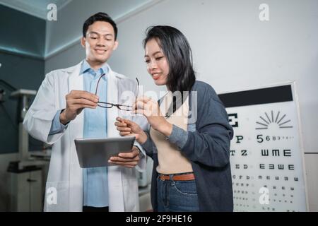 Ein männlicher Arzt gibt der Patientin die Ergebnisse Der Analyse und der Darstellung der empfohlenen Gläser Nach der Überprüfung Stockfoto