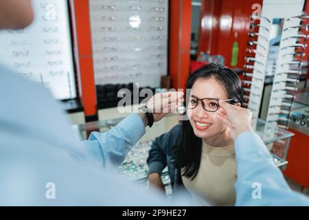 Die Hand eines Mitarbeiters trägt dazu bei, ein Paar anzuziehen Von Brillen, dass eine Frau, die ein Auge getan hat Die Untersuchung wurde ausgewählt Stockfoto