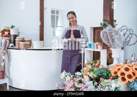 Junge Floristin mit Schürze, die lächelnd vor dem Büro steht und die Kamera anschaut. Stockfoto