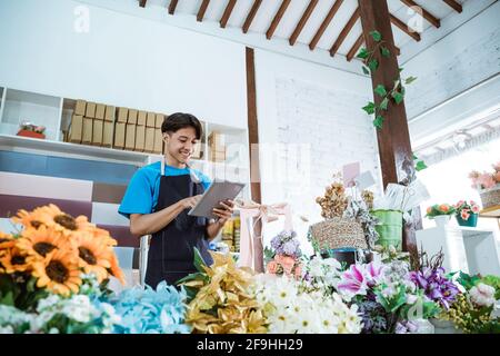 Glücklicher junger Mann Unternehmer, der in einem Blumengeschäft mit Schürze arbeitet Lächelnd Stockfoto