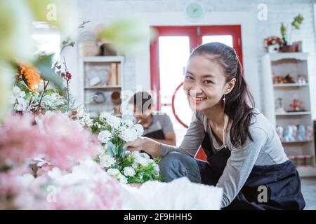 Glückliches junges Paar trägt Schürze lächelnd Blick auf die Kamera. Arbeiten im Blumenladen Stockfoto