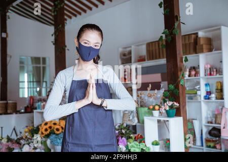 Junge Managerin trägt Schürze und Gesichtsmaske Floristin stehend Grußansage posieren Stockfoto