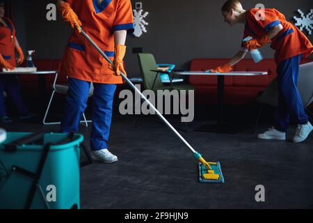 Drei weibliche Hausmeisterinnen in Gummihandschuhen, die die Nassreinigung machen Stockfoto