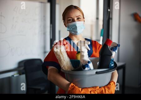 Reinigungskraft in einer Gesichtsmaske, die ihre Reinigungsprodukte zeigt Stockfoto