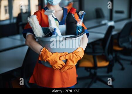 Reinigungskraft in einer Gesichtsmaske, die ihre Reinigungsprodukte zeigt Stockfoto