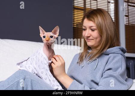 Besitzer in Hausanzug Kleidung Posen auf dem Sofa entspannen mit ihrer Katze in glamourösen und modischen Haustier Kleidung tragen trendigen Körper gekleidet. Stockfoto