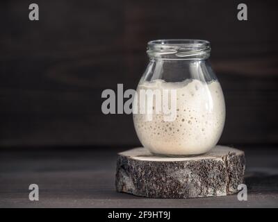 Aktive Weizen-Sauerteig-Starter in Glas auf braunem Hintergrund aus Holz. Starter für Sauerteigbrot. Durchtrainierten Bild. Kopieren Sie Raum. Stockfoto