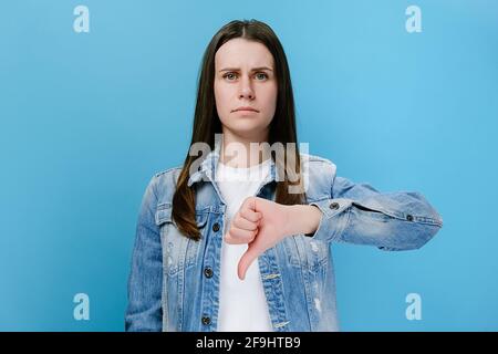 Unzufriedene junge Frau zeigt Daumen nach unten Geste, seriöse Brünette Frau Kunde geben negatives Feedback zu Produkt oder Service Stockfoto