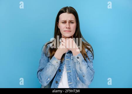 Unglücklich kranke junge Frau berührt den Hals, leidet an Halsschmerzen, hat Asthmaanfall, würgt und grinst Gesicht, isoliert auf blauem Studiohintergrund Stockfoto