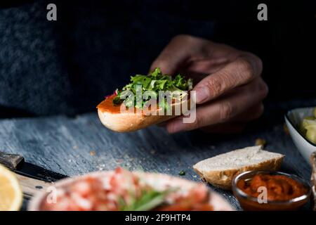 Nahaufnahme eines jungen kaukasischen Mannes, der eine vegane Vorspeise in der Hand hat, die aus einem halbierten gerösteten Brotbrötchen mit einer Tomaten- und Mandelaufstrich, A, hergestellt wurde Stockfoto