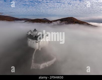 Fuzer, Ungarn - Luftaufnahme des wunderschönen Schlosses von Fuzer, das an einem Herbstmorgen aus dem Nebel mit Zemplen-Bergen und blauem bewölktem Himmel ragt Stockfoto