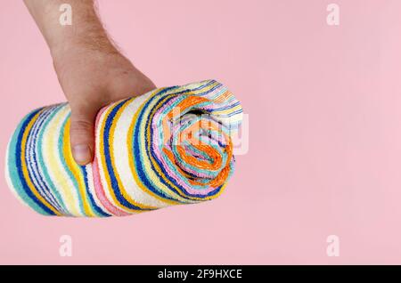 Gestreiftes Handtuch und Hand auf rosa Hintergrund. Mann, der ein buntes Handtuch zusammengerollt hält. Seitenansicht. Selektiver Fokus. Stockfoto