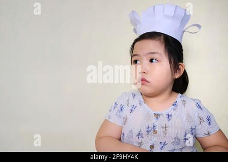 Ein süßes junges molliges asiatisches Mädchen in ihrem Kochkurs, das einen niedlichen Kochhut trägt und leise ihrem Lehrer zuhört. Stockfoto