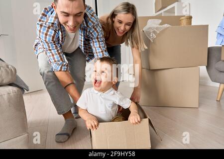 Glückliche Eltern spielen mit niedlichen Kleinkind Kind Sohn Reiten in der Box am bewegenden Tag. Stockfoto