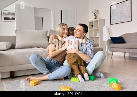 Glücklich junge Familie Paar umarmt niedlichen kleinen Jungen auf dem Boden zu Hause sitzen. Stockfoto