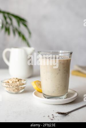 Köstlicher Bananen-Smoothie mit Haferflocken, Kokosmilch und Chiasamen. Gesundes Frühstück, Snack. Einfarbig. Grauer Hintergrund mit grünen Blättern. Vertikal Stockfoto