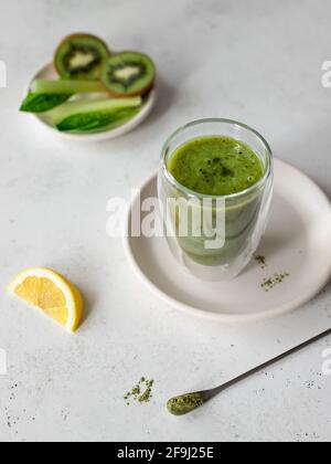 Glas grüner Smoothie mit Spinat, Sellerie, Kiwi, Zitrone und Spirulina. Superfoods und gesunde Ernährung Konzept. Grauer Hintergrund. Draufsicht, vertikal Stockfoto