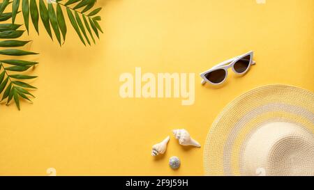 Komposition mit Strandzubehör auf gelbem Hintergrund mit grünem Laub. Strandreisekonzept. Horizontaler Hintergrund mit leerem Platz für Text. Stockfoto