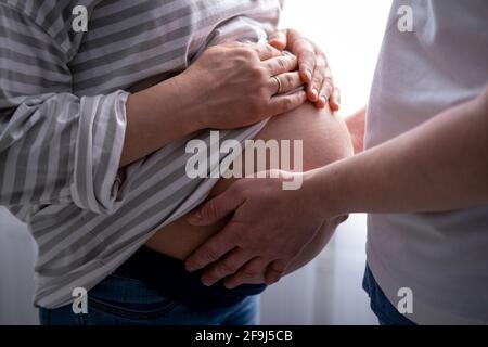 Nahaufnahme Hände auf Mutter und Vater Herz auf schwanger großen Bauch fortgeschrittenen Schwangerschaft. Geliebte Eltern warten Baby Familie Schwangerschaft. Stockfoto
