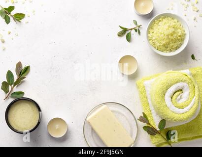 Meersalz, Peeling, feste Seife und Badetücher auf weißem Steingrund mit Kerzen und grünen Blättern. Beauty- und Modekonzept mit Spa-Set. Flat Lay Stockfoto