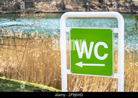 WC-Logo, Zeichen der öffentlichen Toilette vor Naturhintergrund mit Pfeil. Toilette, Waschraum und Badezimmer Stockfoto