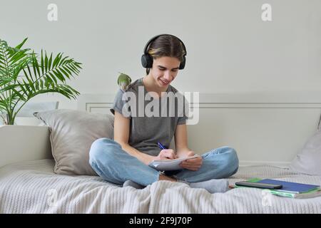 Männlicher Teenager mit grünem Papagei auf der Schulter, mit Lehrbüchern Stockfoto