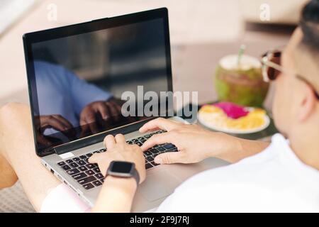 Geschäftsmann ruht sich am Pool aus, isst exotische Früchte und arbeitet am Laptop Stockfoto