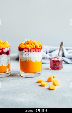Nahaufnahme von zwei Gläsern mit Chia Pudding Kürbismus und Erdbeermarmelade auf grauem Hintergrund Stockfoto