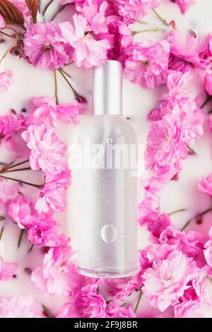 Glasflasche kosmetischen Tonic auf einem Hintergrund von rosa Frühlingsblumen in weißem Wasser oder Milch . Natürliche Bio-Kosmetik-Konzept. Draufsicht, flach liegend, Stockfoto