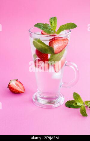 Eingegossen oder entgiftend Wasser mit Erdbeere, Eis und Minze im Glas auf dem rosa Hintergrund. Nahaufnahme. Position vertikal. Stockfoto