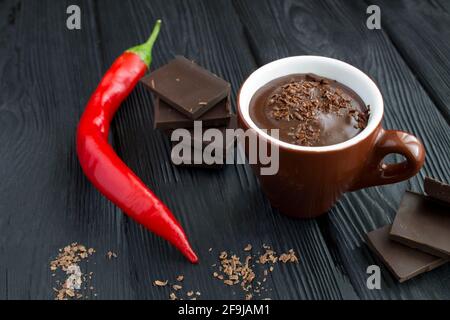 Heiße Schokolade in der braunen Tasse und rote peper-Chili auf dem schwarzen Holzhintergrund. Nahaufnahme. Stockfoto