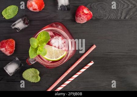 Kalte Limonade mit Erdbeeren und Limette auf dem schwarzen Holzhintergrund. Draufsicht. Speicherplatz kopieren. Stockfoto