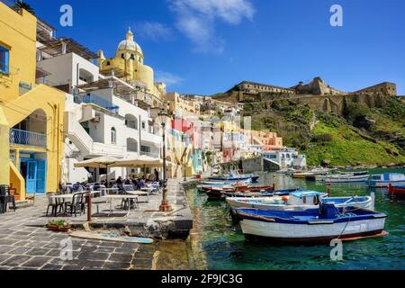 Insel Procida, Neapel, Italien, farbenfrohe Häuser, Fischerboote und Cafés am Meer im Hafen von Marina di Corricella Stockfoto