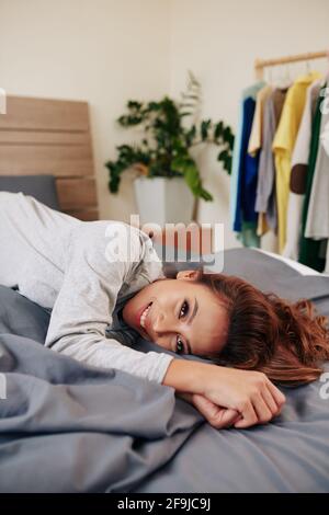 Attraktive lächelnde junge vietnamesische Frau, die sich auf dem Bett entspannt und aussschaut Bei der Kamera Stockfoto