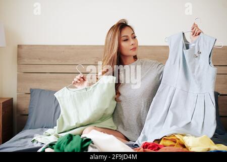 Schöne junge asiatische Frau sitzt auf dem Bett und die Wahl, was Für Veranstaltungen zu tragen Stockfoto