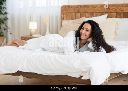 Attraktive junge Frau im Bademantel lächelt im Bett zu Hause Stockfoto