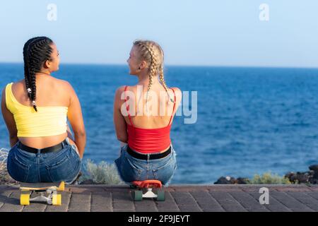 Mädchen sitzen auf dem Skateboard und schauen sich gegenseitig an. Outdoor, urbaner Lebensstil. Relax und Freundschaft Konzept. Stockfoto