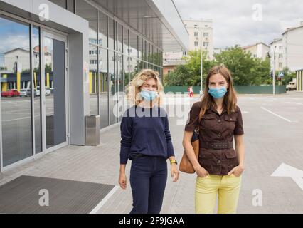 Junge Frauen, Freunde, Kollegen, Schwestern in medizinischen Masken auf der Straße in der Nähe Gebäude des Einkaufszentrums oder Bürozentrum. Städtischer Lebensstil. Konzept der sa Stockfoto