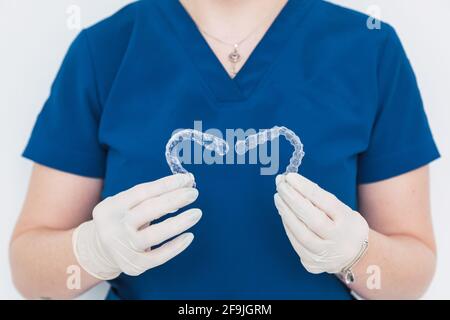 Nicht erkennbarer Arzt, der zwei herzförmige klare Zahnaligner hält. Stockfoto