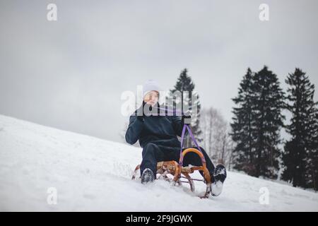 Teenager geritten auf einem Holzschlitten versuchen, seine Richtung mit der Hand zu justieren und sich auf seine Fahrt konzentrieren. Im Winter geht der Athlet unter Stockfoto