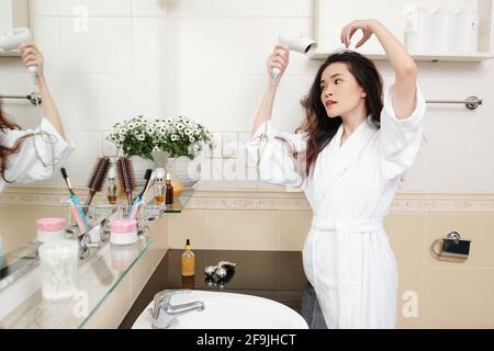 Attraktive junge vietnamesische Frau, die vor dem Haar die Haare ausbläst Badezimmerspiegel Stockfoto