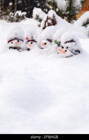 Lustige kleine Schneemänner, die mit frischem Schneefall bedeckt sind und Hüte und Schals und Karottennasen tragen. Winterschnee Spaß und Homour Landschaft mit weißem Raum Stockfoto