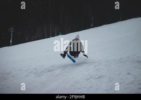 Verrückte Jugend, als wir ähnlichen Unsinn gemacht haben. Ein kleiner Junge auf einem Kunststoff-Snowboard springt auf einen Schneesprung und macht verschiedene Tricks. Geschwindigkeit, Stärke, harter impac Stockfoto