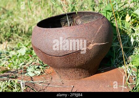 Ein alter gusseiserner Topf steht draußen auf dem Gras. Alte rustikale gusseiserne Utensilien. Schmutziger gusseiserner Topf. Gebrochen in Form eines Lächelns Stockfoto