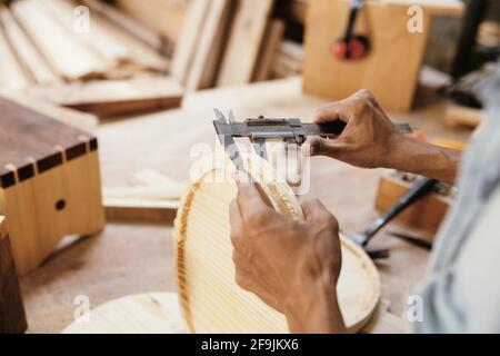 Hände des Zimmermanns, der mit einem Messschieber die Dicke von misst Runde Holzplatte Stockfoto